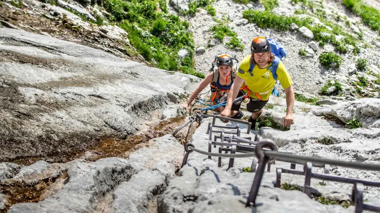Zwei Bergsteiger meistern den Klettersteig Zugspitze. Sie sichern sich mit Seilen an den Eisenstufen, w&auml;hrend sie den steilen Fels erklimmen.