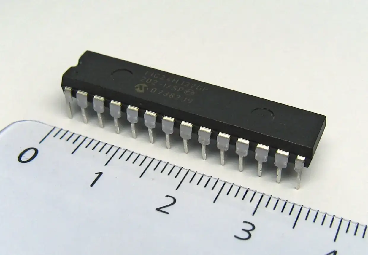 Mikroprocesor PIC24HJ32GP, kluczowy element dla każdego programatora, leży obok linijki.