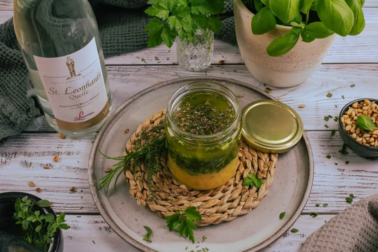 Frisches Salatdressing mit Kräutern im Glas, daneben eine Flasche St. Leonhards Quelle und frische Kräuter.
