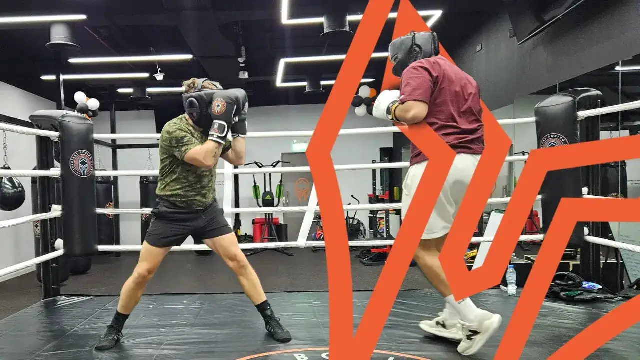 Two boxers in headgear and gloves spar in a ring, practicing amateur boxing rules.
