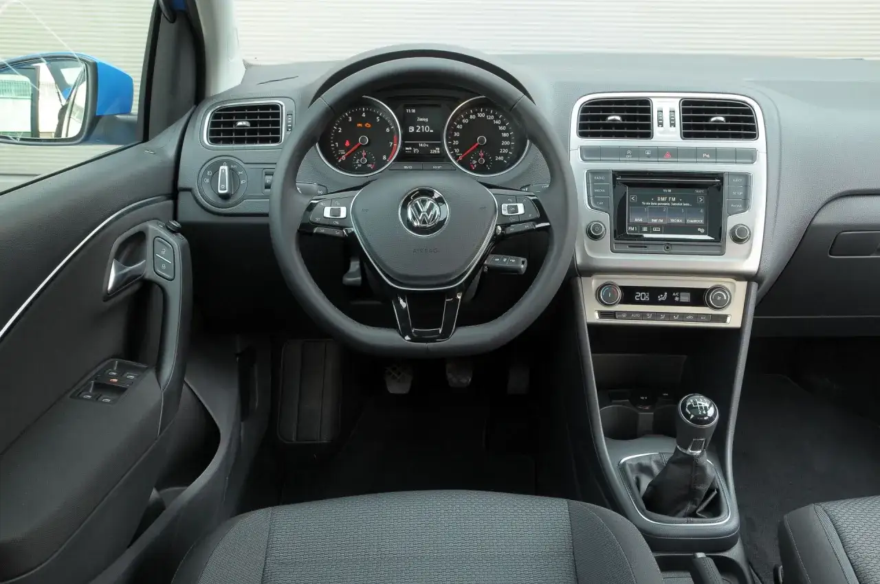 Wnętrze Volkswagena Polo 6: kierownica, deska rozdzielcza z radiem i klimatyzacją, dźwignia zmiany biegów.