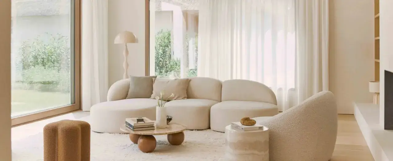 Soggiorno luminoso con divano curvo, tavolino rotondo e pouf in stile moderno. Un esempio di come arredare case moderne con eleganza e comfort.