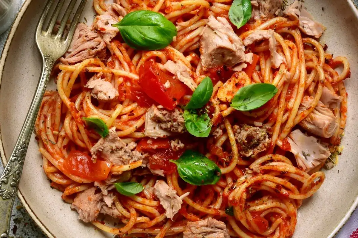 Spaghetti al sugo di pomodoro con abbondante tonno in scatola, guarniti con foglie di basilico fresco. Un piatto semplice e gustoso.
