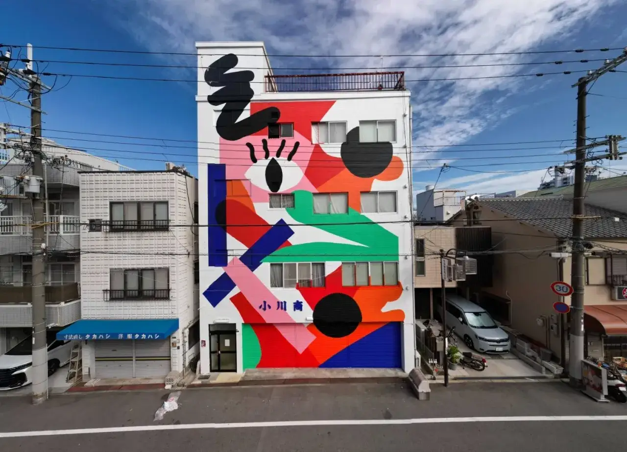 Vibrant street art style mural adorns a building facade with abstract shapes and bold colors, creating a lively urban scene.