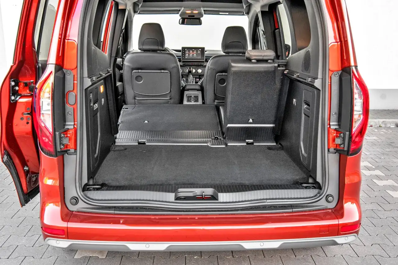 Wnętrze czerwonego Renault Kangoo 1.5 dCi z otwartą klapą bagażnika. Widoczne rozłożone tylne siedzenia i duża przestrzeń ładunkowa.