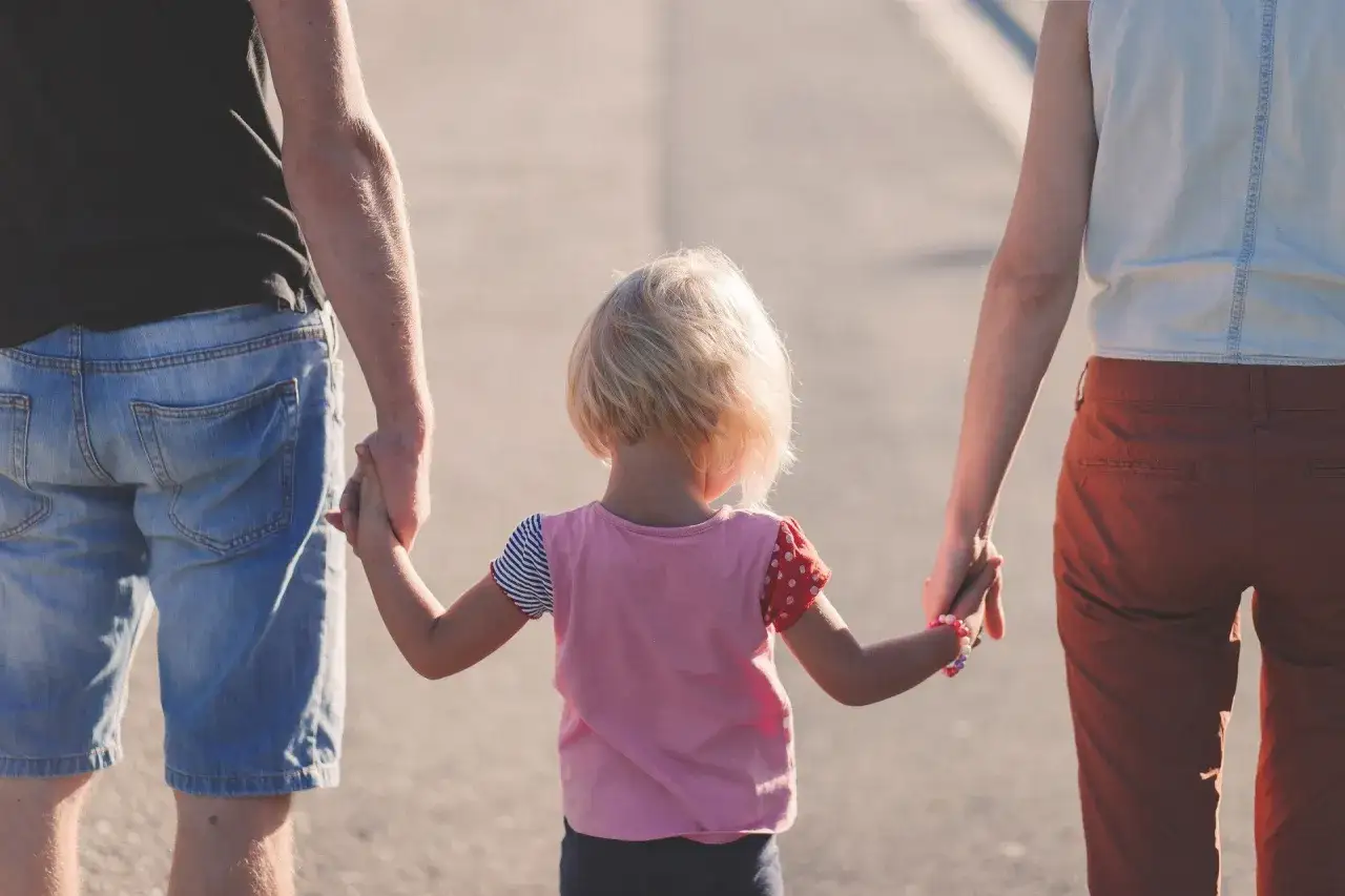 Rodzice prowadzą dziecko za rękę. Wsparcie i miłość to podstawa rozwoju, jak w oligofrenopedagogice.