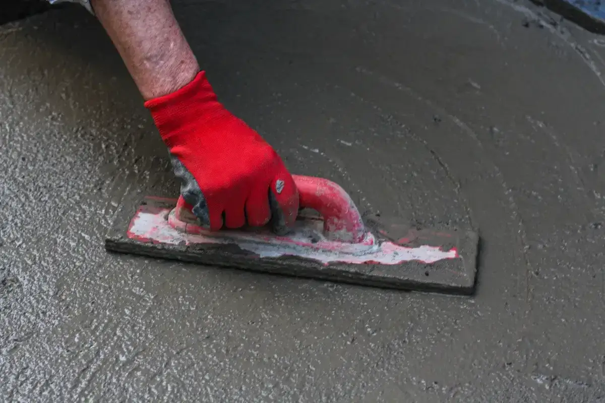 Ręka w czerwonej rękawicy wygładza świeży beton kielnią. To kluczowy etap, jak wylać beton na podjazd, by był równy i trwały.