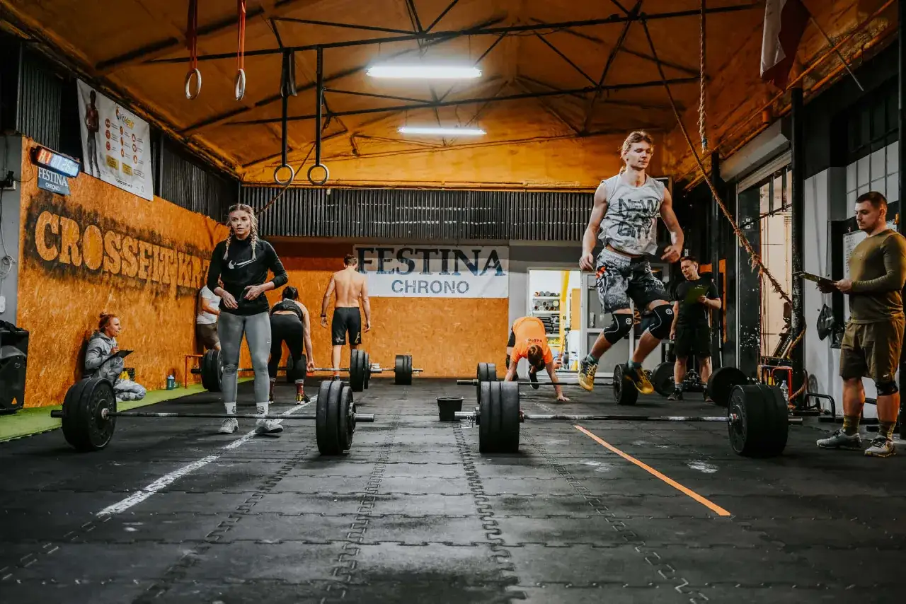 Trening crossfit we Wrocławiu. Ludzie ćwiczą z ciężarami, skaczą i podnoszą sztangi.