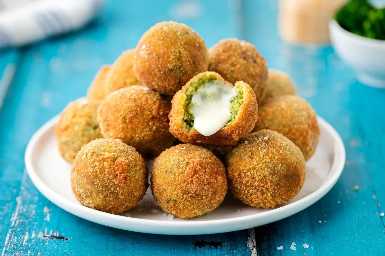 Un mucchio di polpette di broccoli dorate e croccanti, una delle quali è aperta rivelando un cuore filante di formaggio.