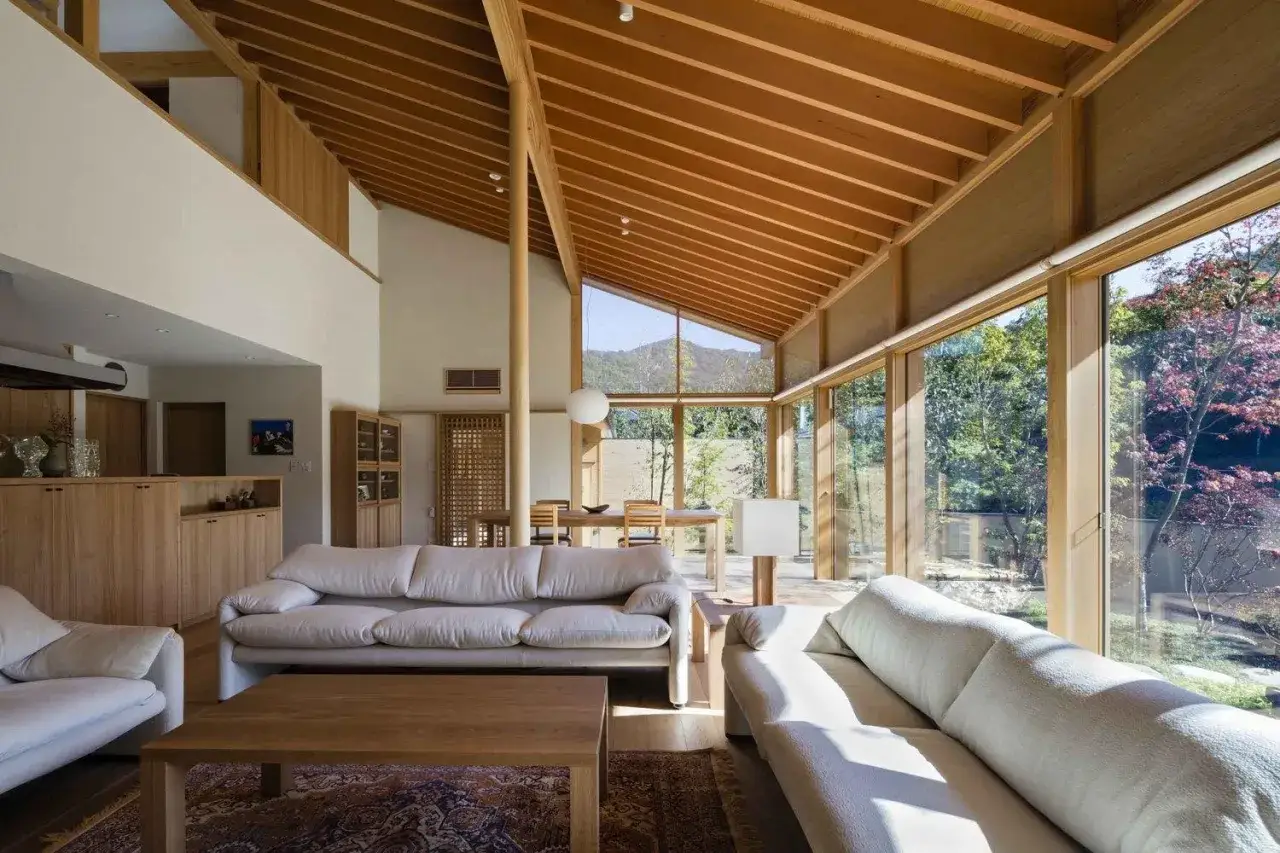 Salon lumineux d'une maison style japonais en France, avec canapés blancs, bois apparent et grandes baies vitrées donnant sur un jardin luxuriant.