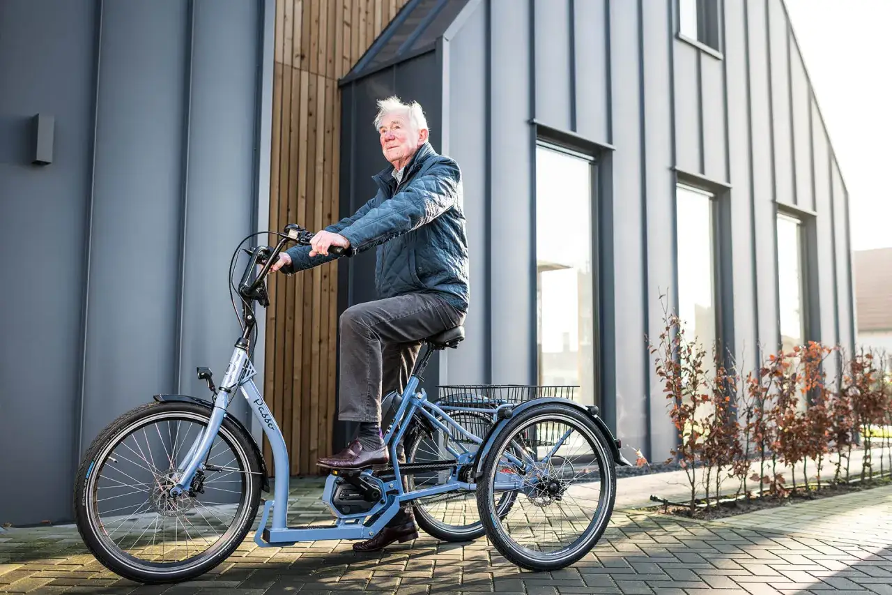 Een oudere man geniet van een ritje op zijn driewieler, een bejaarden fiets, voor een moderne woning.