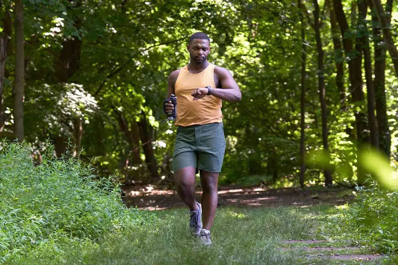 Uomo corre nel bosco, controlla l'orologio per monitorare quante calorie si bruciano al giorno.