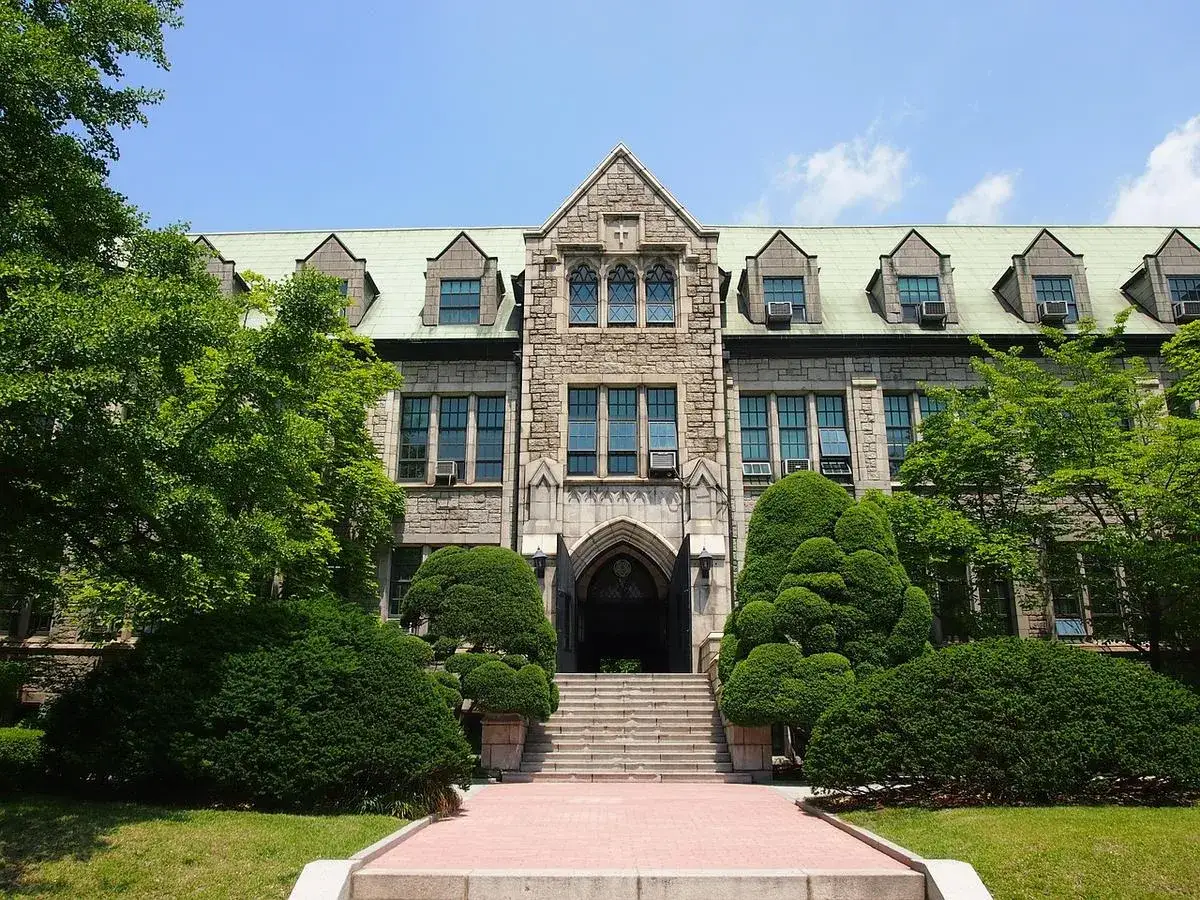 Bâtiment en pierre de style ancien, avec des arbres verts luxuriants devant. C'est la **Korea University Business School**.