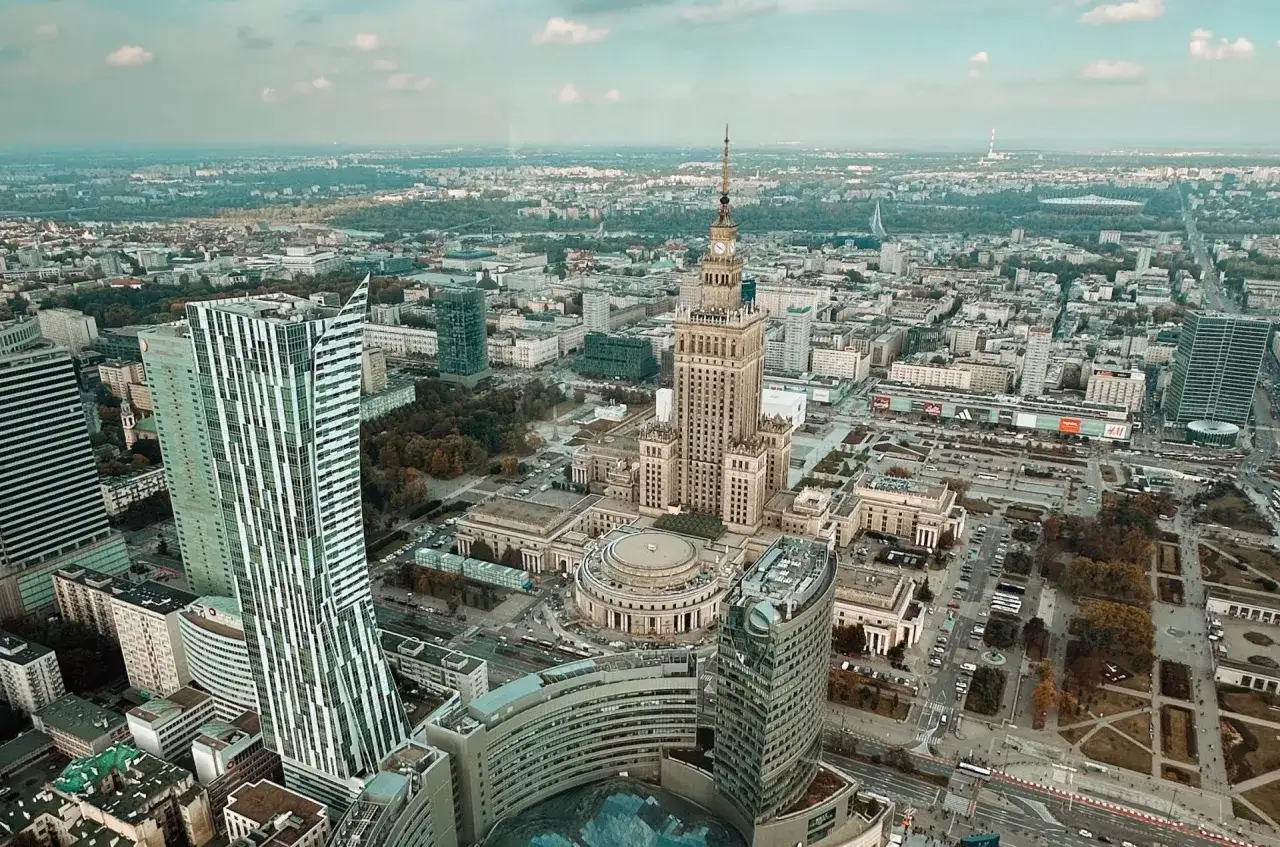 Widok na Pałac Kultury i Nauki, najwyższy budynek w Polsce, otoczony nowoczesnymi wieżowcami i zielenią miejską.