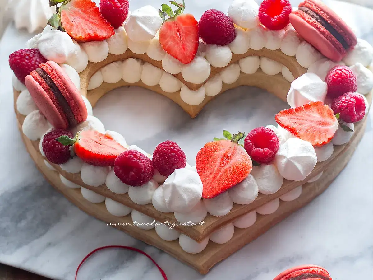 Cuore di pasta biscotto per torte a strati, decorato con panna, fragole, lamponi e macarons.