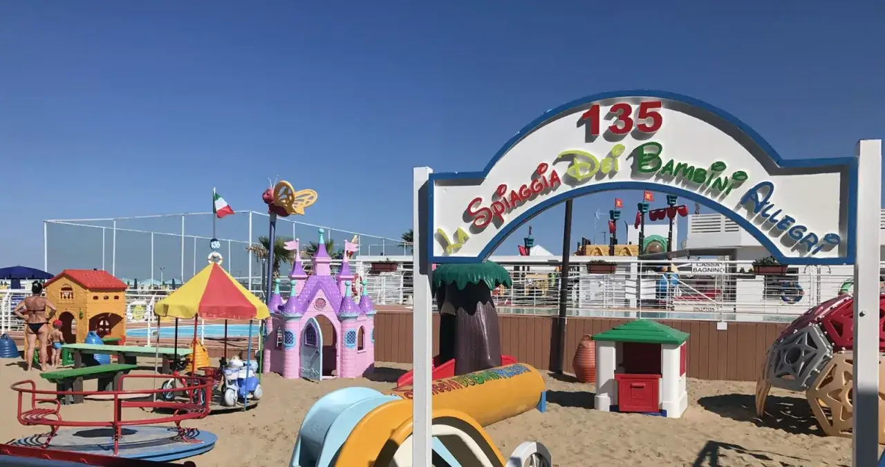 Area giochi per bambini al Bagno 19 Riccione: castello, casetta, giostra e scivoli sulla sabbia.