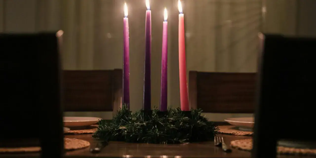 Four lit candles, three purple and one pink, sit on a wreath for the first Sunday of Advent readings.