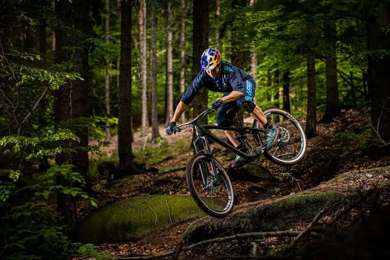Rowerzysta zjeżdża po leśnej ścieżce, pokonując przeszkody. Ekscytujące trasy rowerowe w górach czekają na śmiałków.