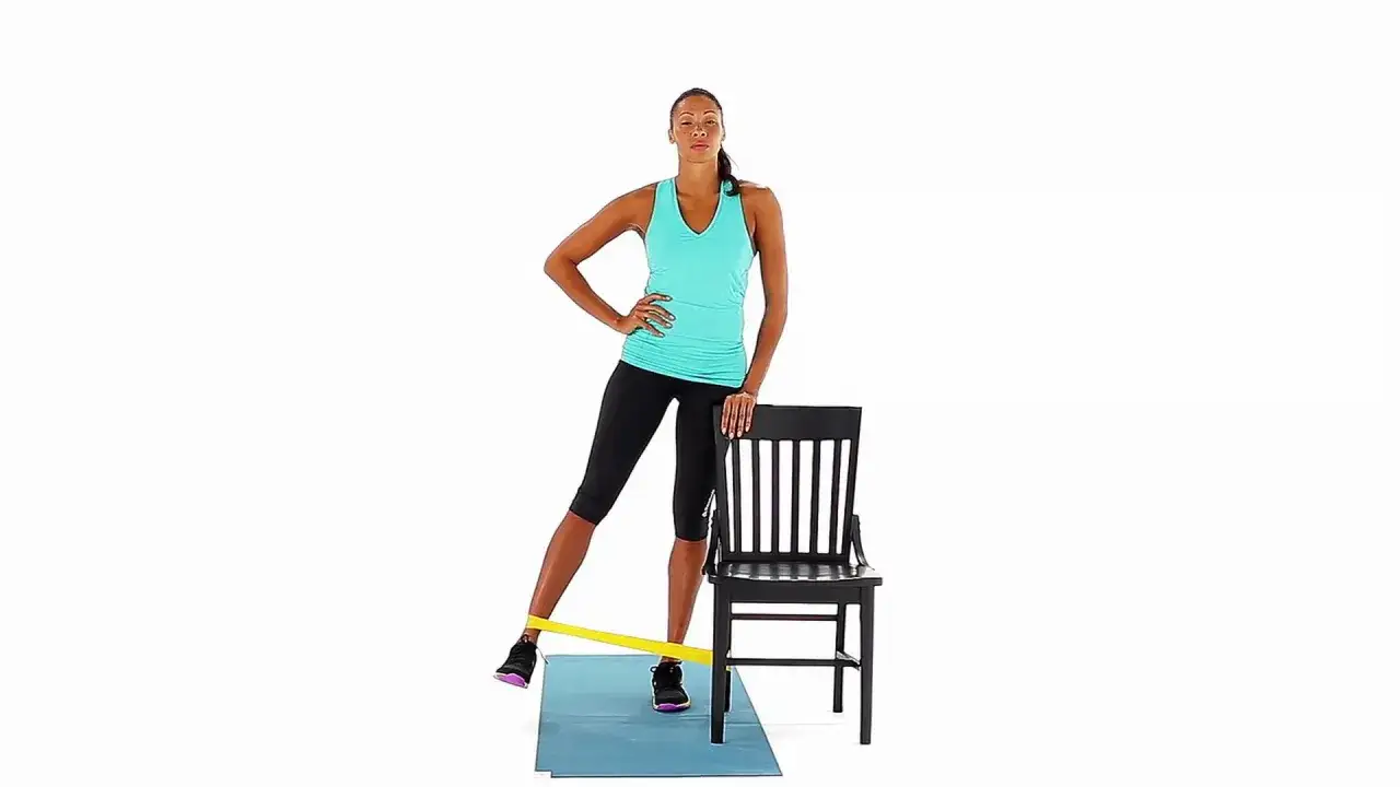 Femme effectuant un moyen fessier exercice avec une bande de résistance, s'appuyant sur une chaise pour l'équilibre.