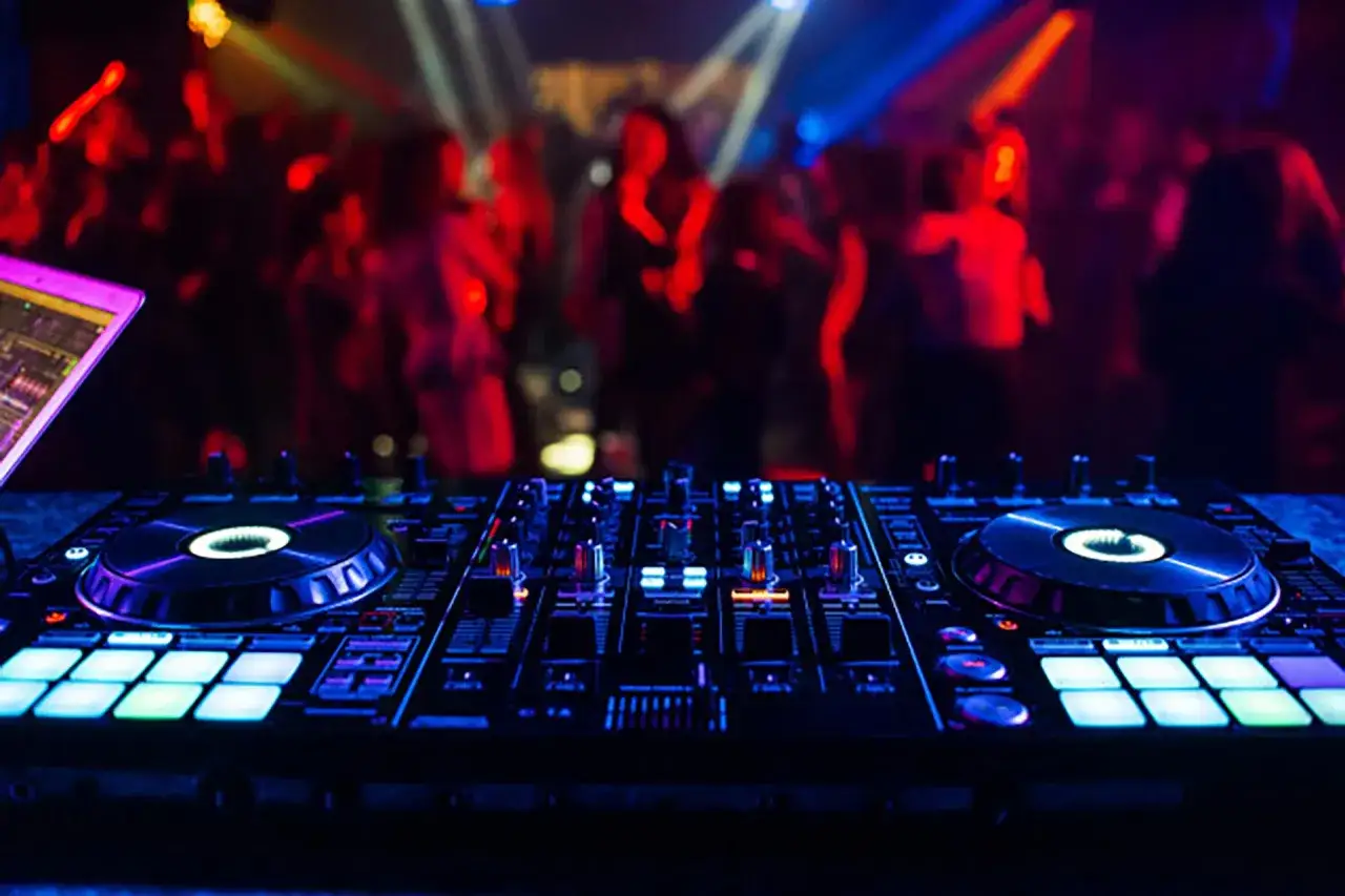 DJ-Controller Pioneer XDJ RX3 im Fokus, im Hintergrund tanzt eine Menge im Club.