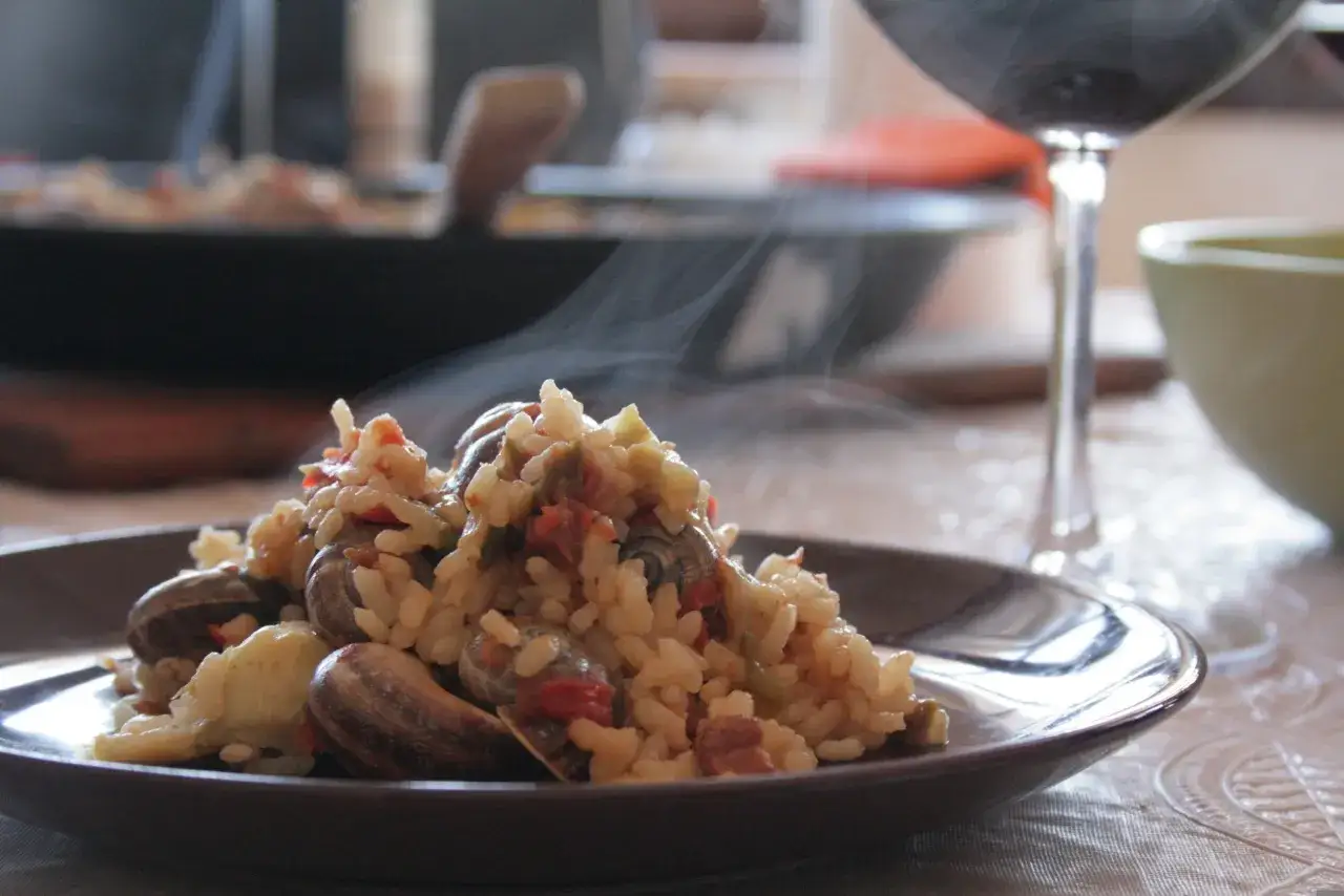 En ångande portion paella med sniglar och ris, perfekt ackompanjerad av ett glas rött vin.