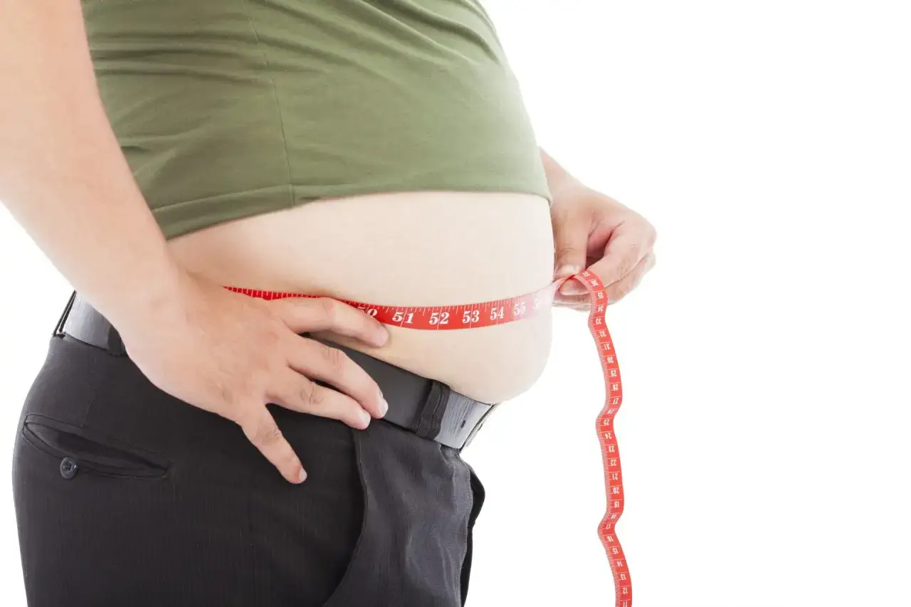Mann misst seinen Bauch mit einem Ma&szlig;band. Der Wunsch, den Bauch zu kaschieren, wird durch die Messung deutlich.