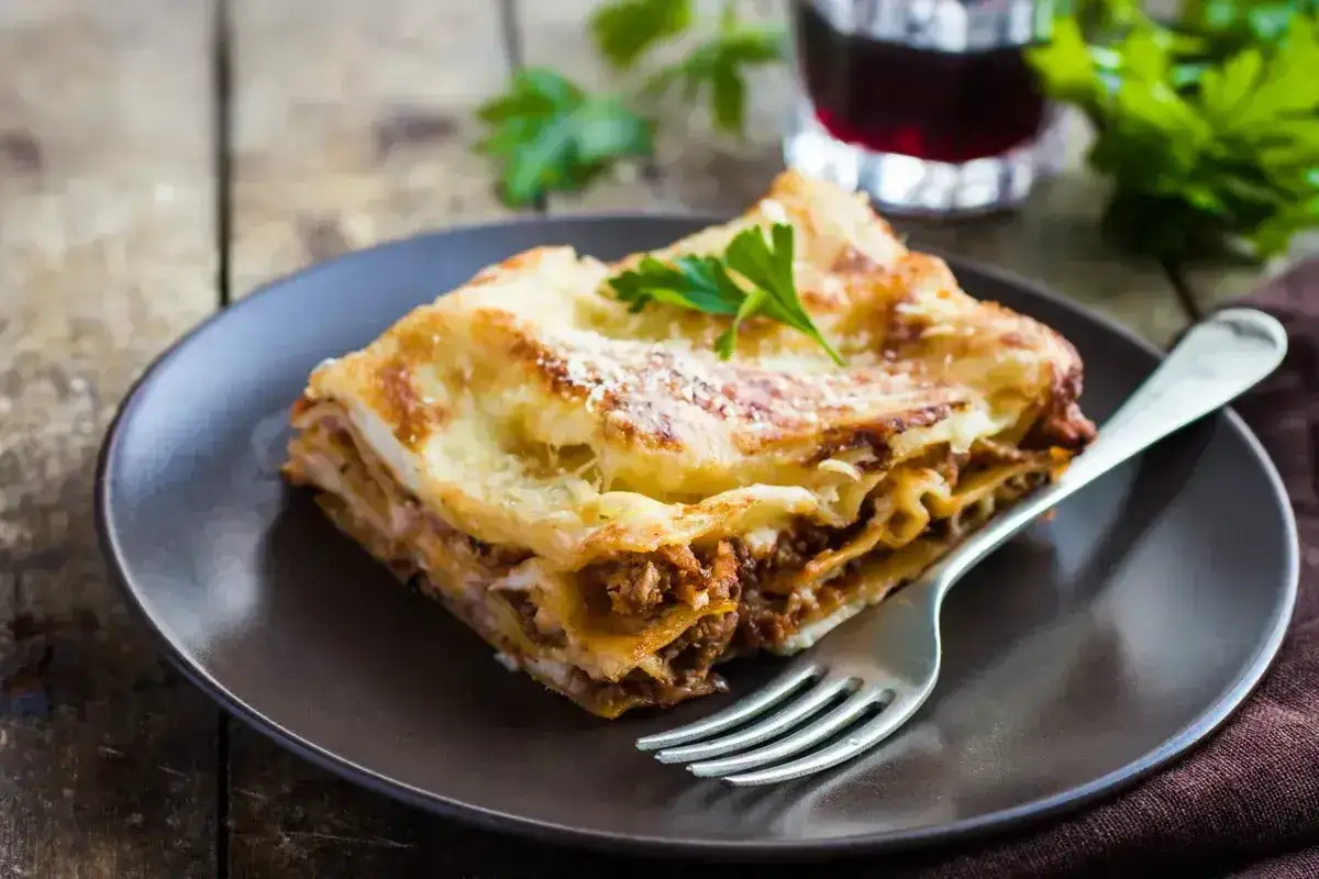 Pyszny kawałek lasagne z mięsem i serem, udekorowany natką pietruszki, czeka na widelcu. Idealny na obiad.