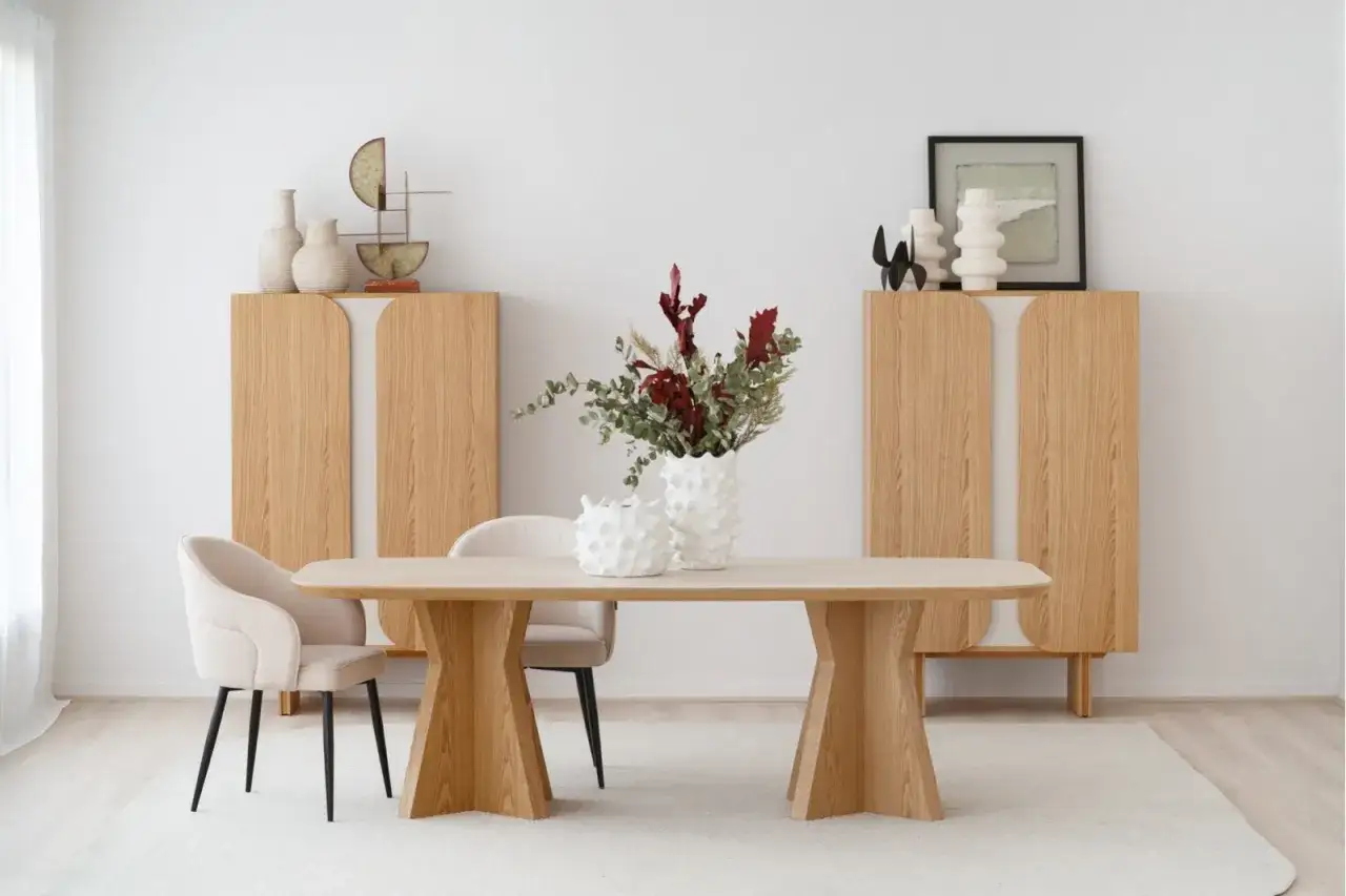 Un comedor moderno con coberts a taula, dos armarios de madera, sillas tapizadas y un jarrón con flores.