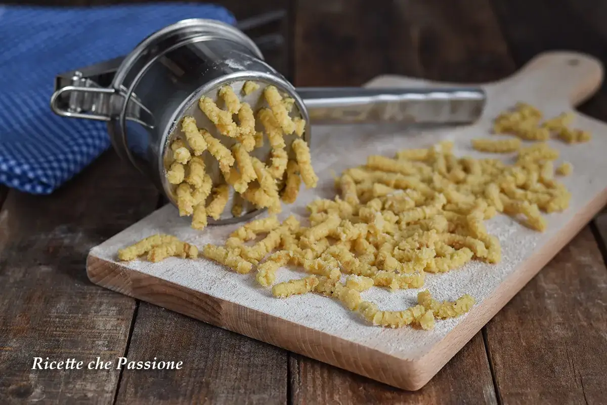 Passatelli marchigiani appena fatti, estrusi da un attrezzo su un tagliere di legno. La ricetta è pronta per essere gustata.