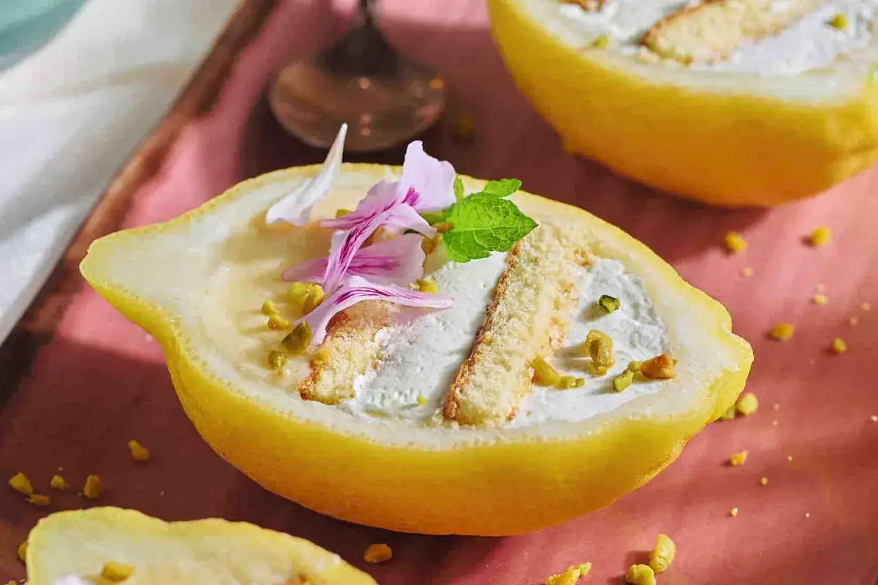 Delizia al limone: un dolce fresco servito in un limone scavato, guarnito con panna, biscotti, pistacchi e fiori rosa.