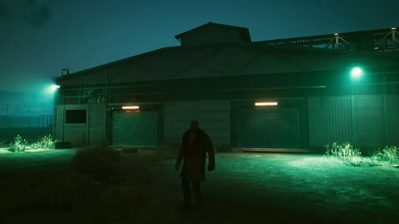 Mężczyzna w płaszczu stoi przed magazynem w nocnej scenerii. To kwestia czasu, zanim cyberpunkowa rzeczywistość pochłonie to miejsce.