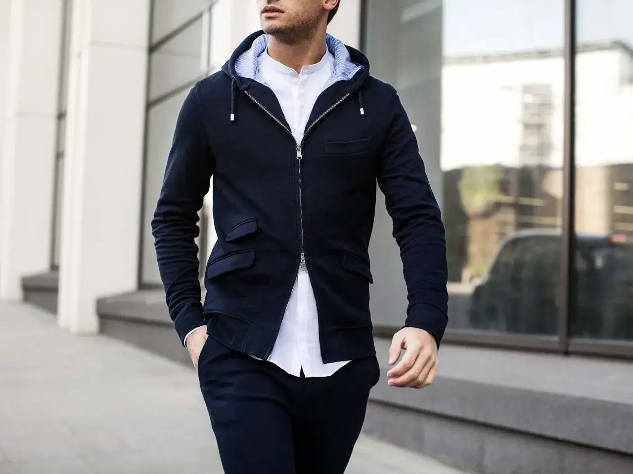 Sebastian Dollinger i m&ouml;rkbl&aring; hoodie och vit skjorta, med handen i fickan, g&aring;r l&auml;ngs en byggnad.