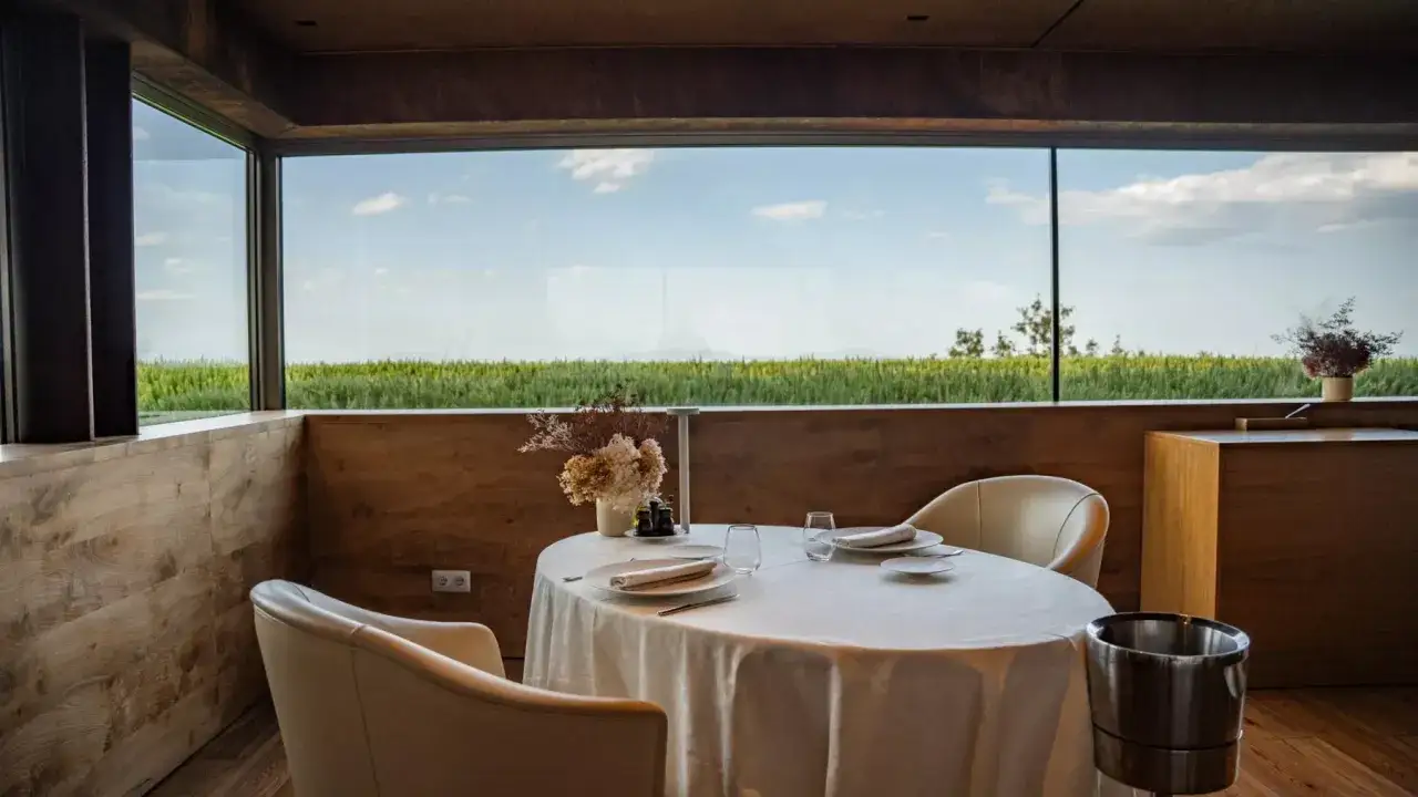 Mesa elegante en uno de los mejores restaurantes de España, con vistas a campos verdes y cielo azul.