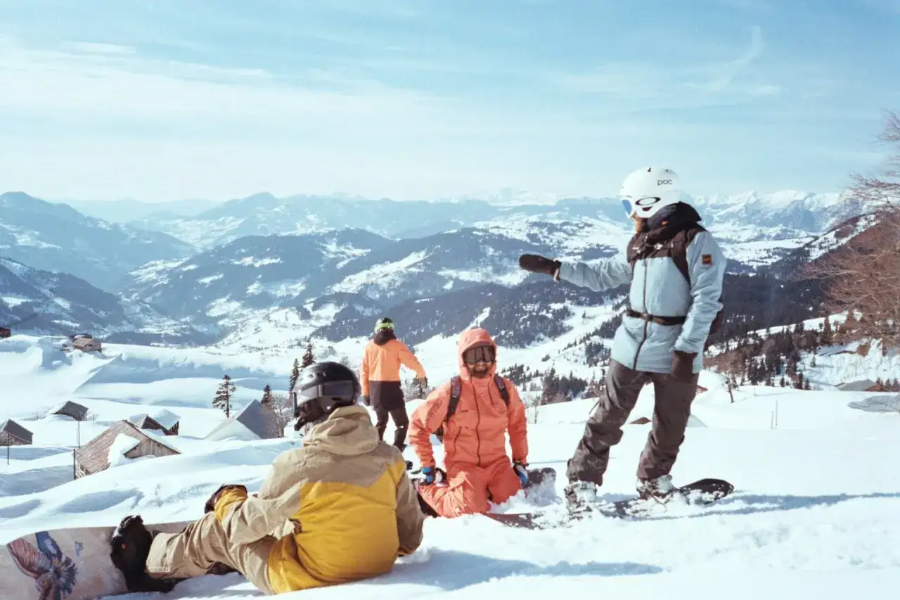 Grupa snowboardzist&oacute;w na stoku, w tle g&oacute;ry. Pamiętaj o ubezpieczeniu narciarskim Polska, by cieszyć się zimową przygodą bez obaw.