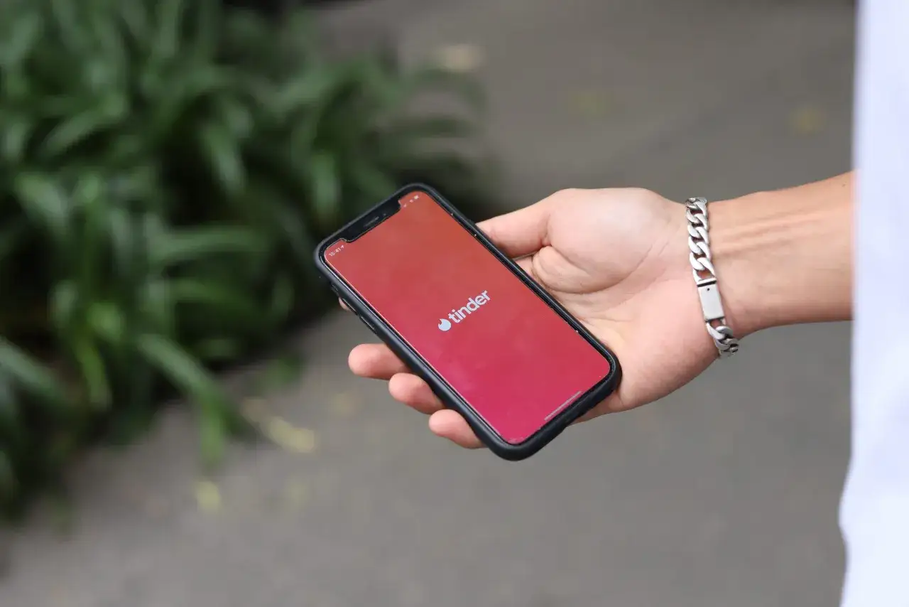 Dłoń trzyma smartfon z logo Tinder. Zastanawiasz się, ile lajków dziennie możesz zdobyć?
