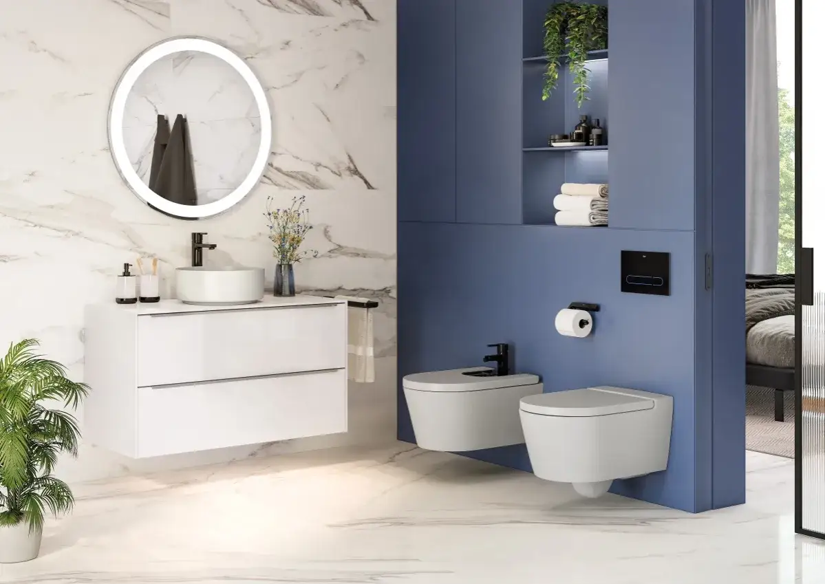 Nowoczesna, **oryginalna łazienka** z białymi meblami, okrągłym lustrem i niebieskimi akcentami. Widoczne dwie wiszące toalety i bidet.
