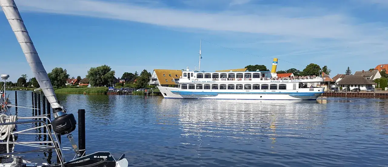 Ein Ausflugsschiff mit vielen Passagieren fährt im breege hafen. Im Vordergrund ist ein Segelboot zu sehen.