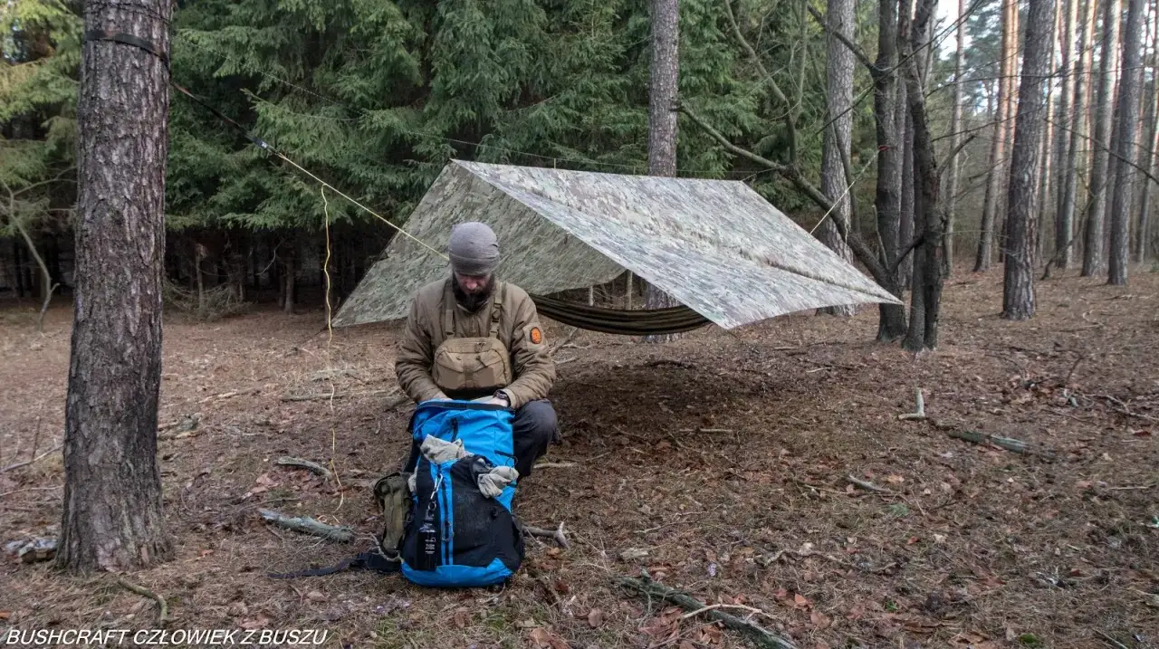 Człowiek w lesie przygotowuje się do biwaku. Rozbity tarp, hamak, plecak – to esencja bushcraftu.