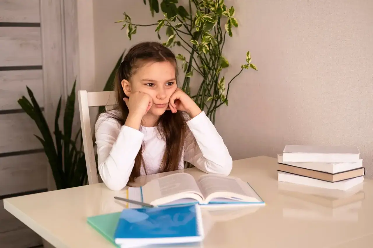 Dziewczynka zamyślona nad książką, być może zmaga się z dysleksją i dysortografią, co utrudnia jej naukę.