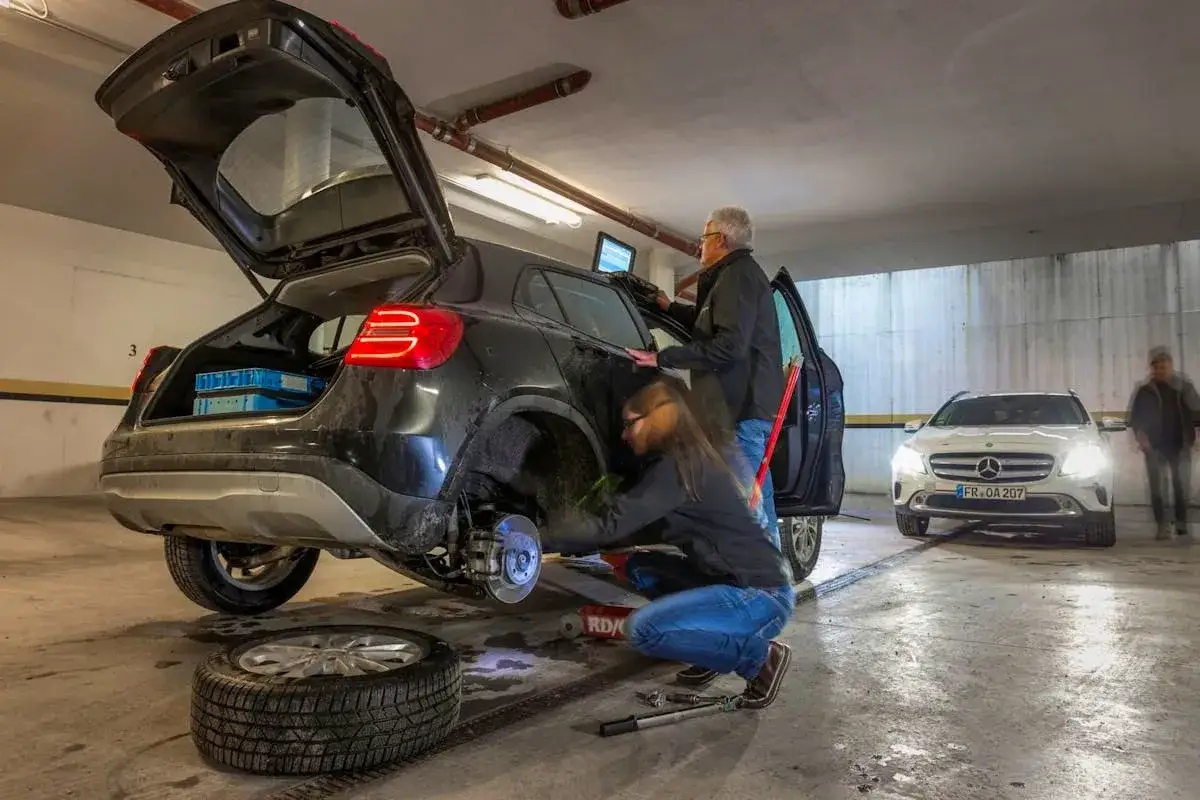 Un couple change une roue crevée. Ils sont en train de rouler avec une roue de secours dans un parking.