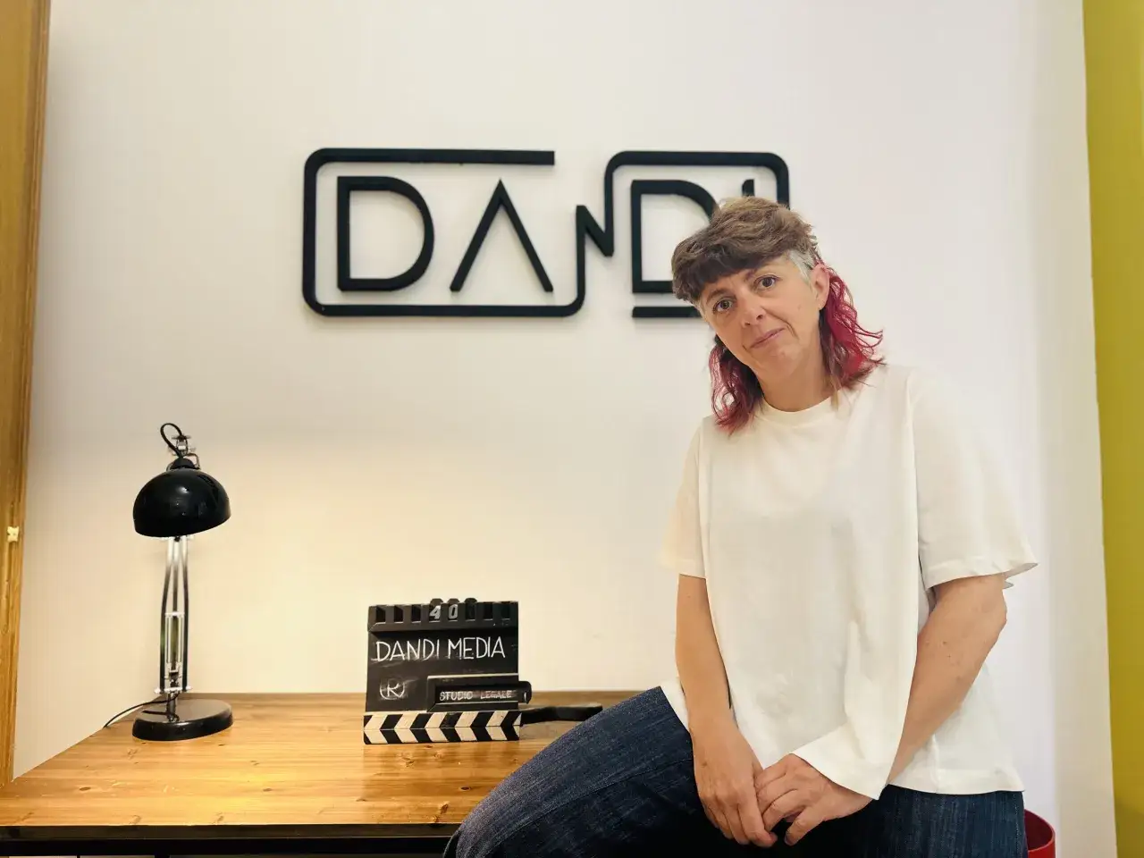 Donna con capelli rossi e grigi, seduta vicino a un ciak