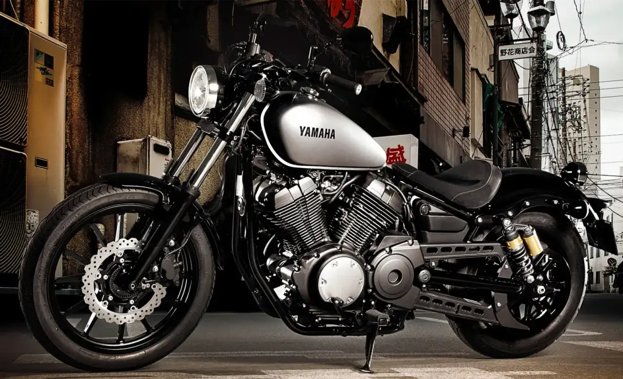 Stylowy motocykl Yamaha XV950 z chromowanymi elementami i czarnym lakierem, zaparkowany na ulicy w azjatyckim mieście.