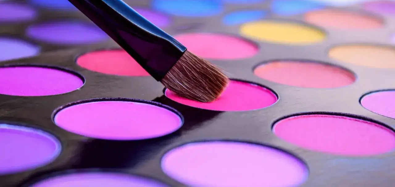 Pinsel ber&uuml;hrt leuchtend pinken Lidschatten in einer Palette mit vielen bunten Farben, wie CI 45410.