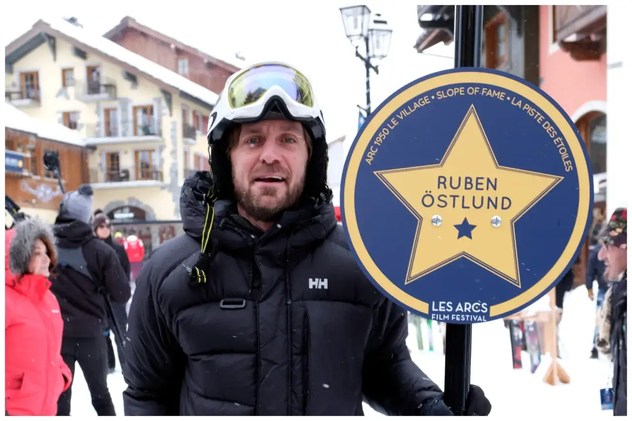 En skid&aring;kare med skidglas&ouml;gon och en HH-jacka st&aring;r bredvid en skylt f&ouml;r 