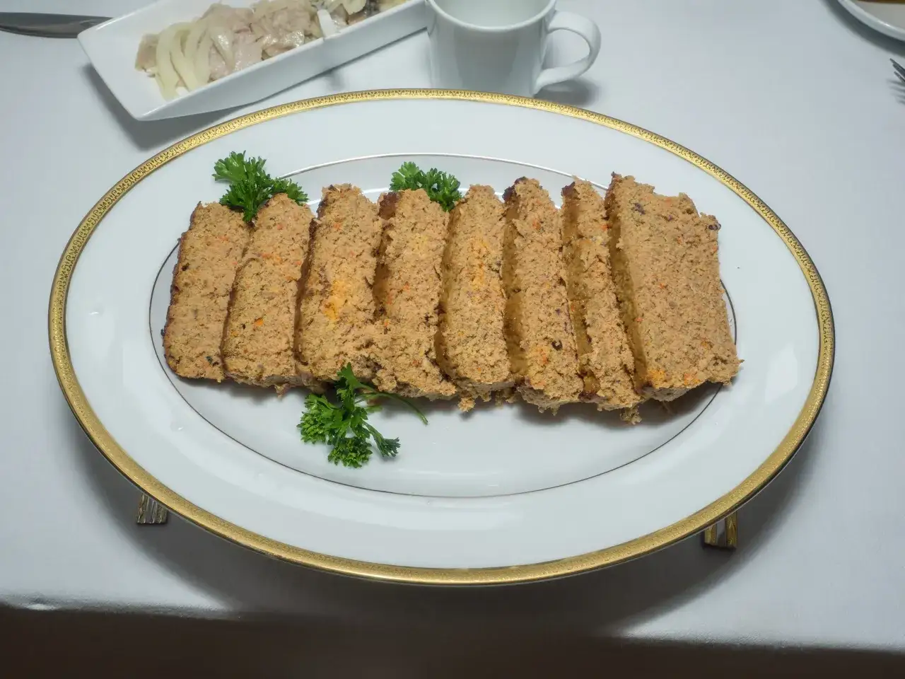 Pokrojony pasztet drobiowo-wieprzowy z wątróbką, udekorowany natką pietruszki, podany na eleganckiej tacy.