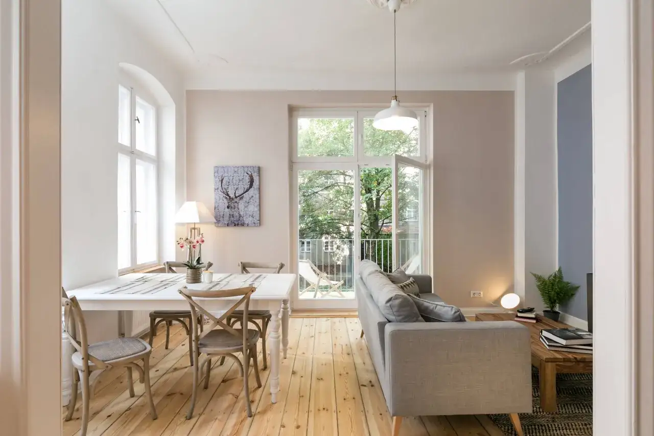 Helles 15 qm Wohnzimmer mit Essbereich einrichten: Weißer Esstisch, graue Stühle, Sofa, Holzboden, Fenster mit Blick ins Grüne.