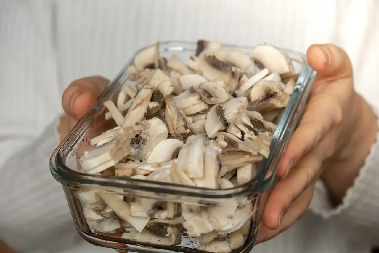 H&auml;nde halten Glasbeh&auml;lter mit geschnittenen Champignons, bereit zum Einfrieren.