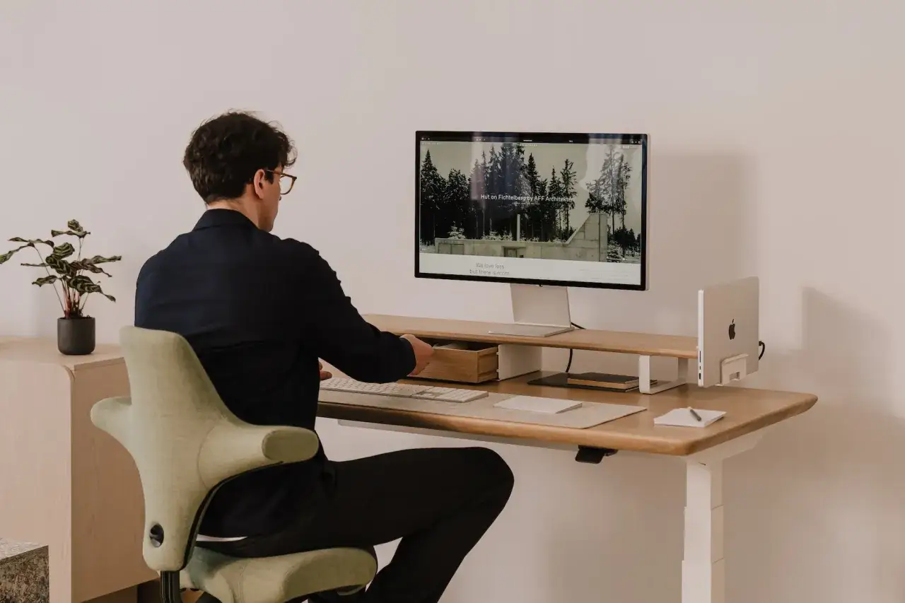Un homme porte des lunettes et travaille sur son ordinateur. Il est assis sur une chaise ergonomique, une plante verte à côté de lui. Il est important de savoir comment protéger ses yeux des écrans.