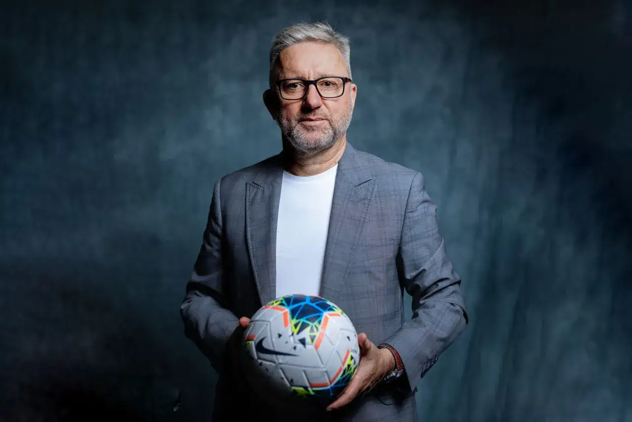 Doświadczony trener U21 w eleganckim garniturze trzyma piłkę nożną, gotowy do poprowadzenia młodych talentów.