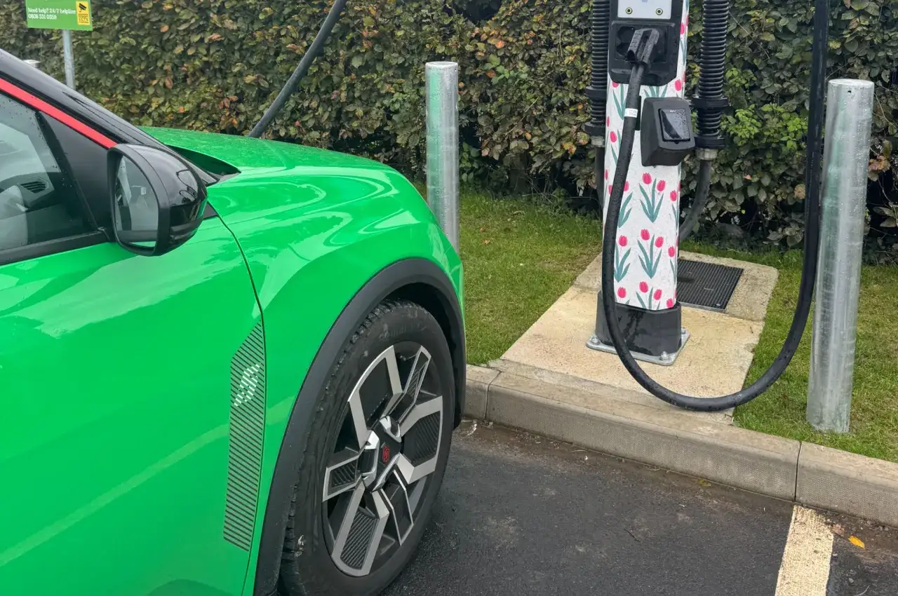 Zielony Renault 5 Electric ładuje się przy stacji z tulipanami.